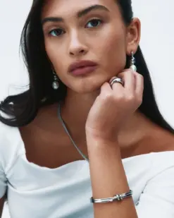 Detaljbild av swirl-designade rostfria örhängen med pärla